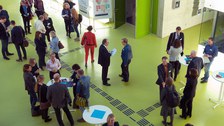 Bild des Foyers der Fakultät Informatik an der TU Dresden. Zu sehen sind mehrere Personen, die teilweise um Stehtische herum gruppiert sind und sich augenscheinlich unterhalten.