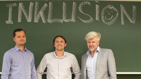 Foto von drei männlichen Personen vor einer Tafel, auf der mit Kreide das Wort "Inklusion" geschrieben steht