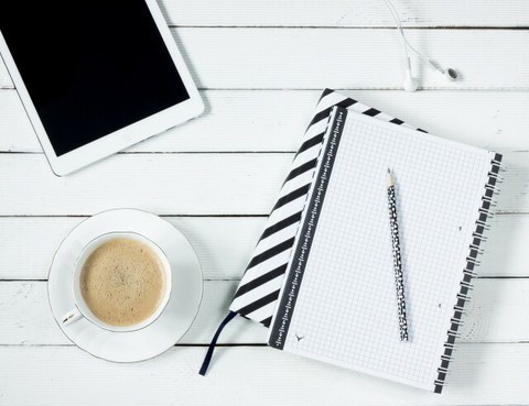 Foto: Auf einem Tisch liegt ein Tablet, ein Notizblock und steht eine Tasse Kaffee