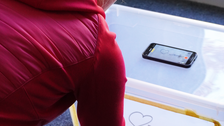 Eine Frau erstellt an einer Trickfilmbox einen Erklärfilm. Man sieht sie von hinten an der Box hantieren. Sie trägt einen roten Pulli und hat blonde Haare.