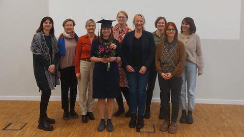 10 Personen stehen vor einer weißen Wand, die eine Präsentation zeigt.