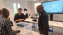 Frau erklärt zwei Männern die Legetechnik für ein Erklärvideo mithilfe einer Plastikbox und eines Tablets
