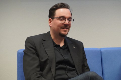 Mann sitzt auf Sofa und diskutiert dabei