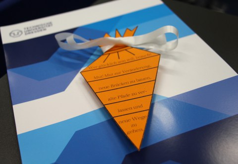 Abgebildet ist eine flache Papier-Schultüte mit schriftlichen guten Wünsche für die wissenschaftliche Ausbildung.