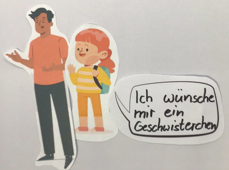 Auf dem Bild, das mit Papierfiguren für die Legetechnik entstanden ist, sieht man ein Mädchen, das zu ihren Papa in einer Sprechblase sagt: "Ich wünsche mir ein Geschwisterchen"