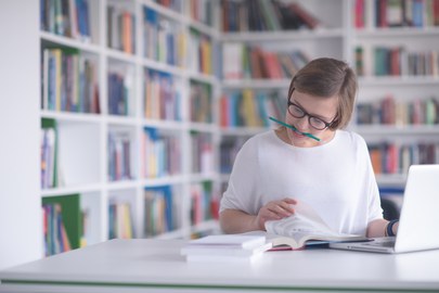 Frau arbeitet mit Buch und Laptop an einem Schreibtisch