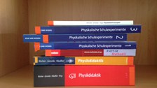 Bild von Physikbüchern, die in einem Holzregal gestapelt sind.