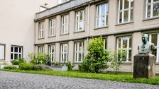 Bild einer Hausansicht des Physikgebäudes "Recknagel-Bau" an der TU Dresden. Zu sehen ist das Gebäude, davor ein Weg mit Grünfläche und einer Büste.