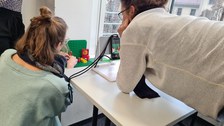 Drei Personen betrachten ihre Video-Szene, die mit Spiel-Figuren auf einem Tisch aufgebaut wurde. Sie blicken durch eine Smartphone-Kamera auf die aufgebaute Szene.