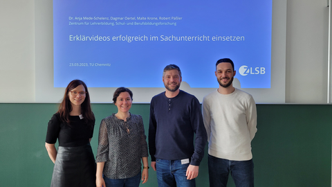 Das Workshop-Team, bestehend aus Dr. Anja Mede-Schelenz, Dagmar Oertel, Robert Päßler und Malte Krone stehen vor einer Tafel mit der Titelfolie ihres Workshops, die den Titel trägt: "Erklärvideos erfolgreich im Sachunterricht einsetzen"