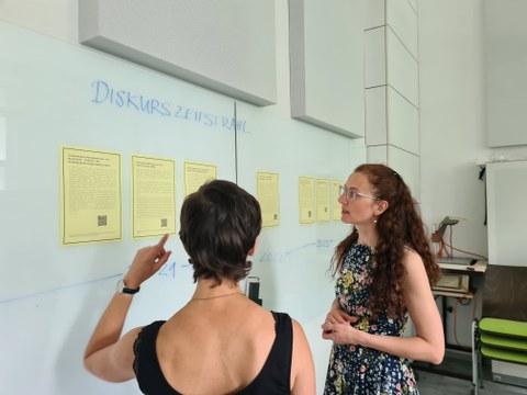 Zwei Frauen stehen vor einem Whiteboard und sprechen miteinander.