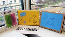 Man sieht zwei verschiedene bunte Lernkisten, die auf einem Tisch stehen und vor ein Fenster an der DIU gelehnt sind, sodass man im Hintergrund den Blick nach draußen bekommt.