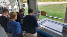 SuS die neben einem Lasercutter stehen und an einem PC eine Visitenkarte gestalten