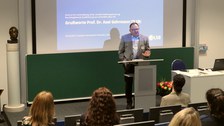 Auf dem Bild ist Herr Prof. Dr. Gehrmann (Geschäftsführender Direktor ZLSB) bei der feierlichen Verabschiedung zu sehen, wie er eine Rede im Hörsaal an der DIU hält.