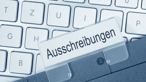 Foto zeigt eine Tastatur, auf der ein Ordner liegt zum Thema "Ausschreibungen".